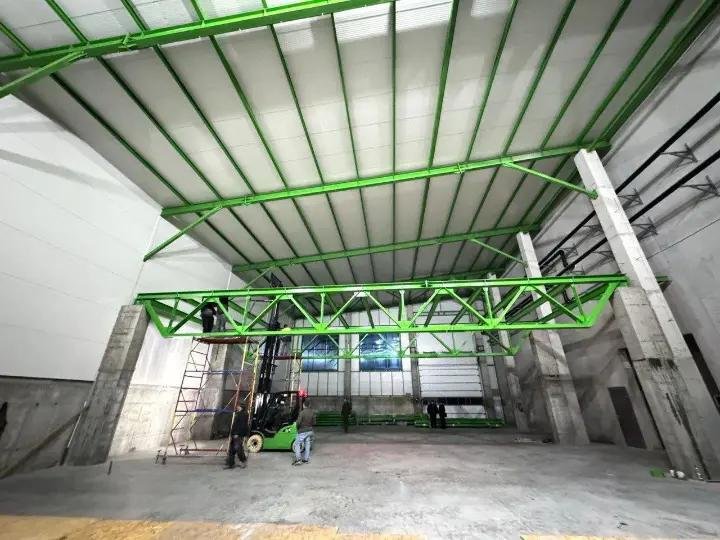 Fermă metalică verde montată în interiorul unei hale